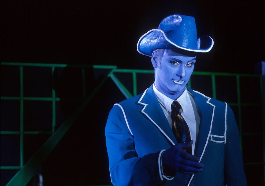 A blue person with a cowboy hat looks at the camera.